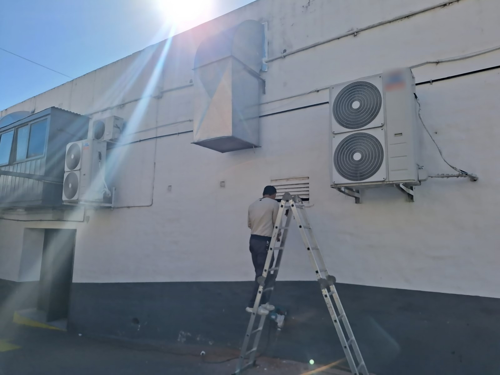 Técnico de LC - Servicios Técnicos trabajando sobre una escalera junto a equipos de aire acondicionado instalados en la pared de un edificio